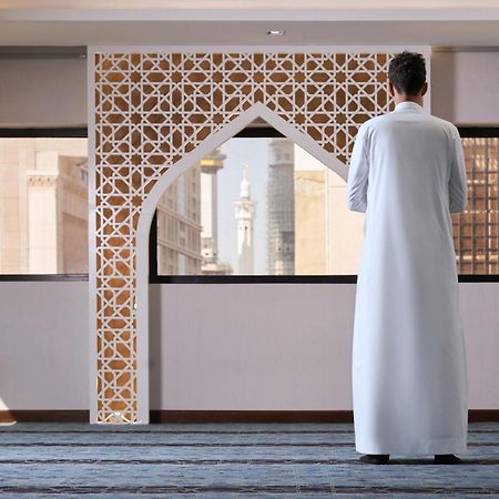 Makarem Ajyad Makkah Hotel La Meca Exterior foto The photo depicts a person standing with their back facing the viewer, wearing a traditional white garment. They are in a spacious interior setting that features an ornate archway with intricate patterns, typical of Islamic architecture. Through the 