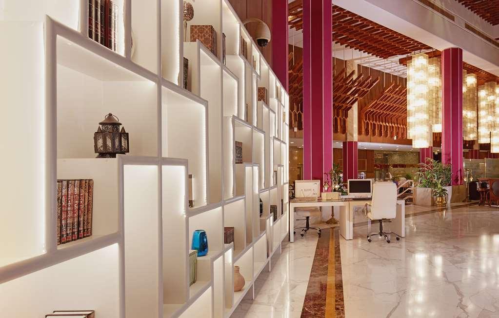 Makarem Ajyad Makkah Hotel La Meca Interior foto The photo shows a modern interior space, likely a lobby or lounge area of a stylish hotel or building. There is a partition wall made up of white shelving units illuminated from within, displaying various decorative items, books, and vases. The desig