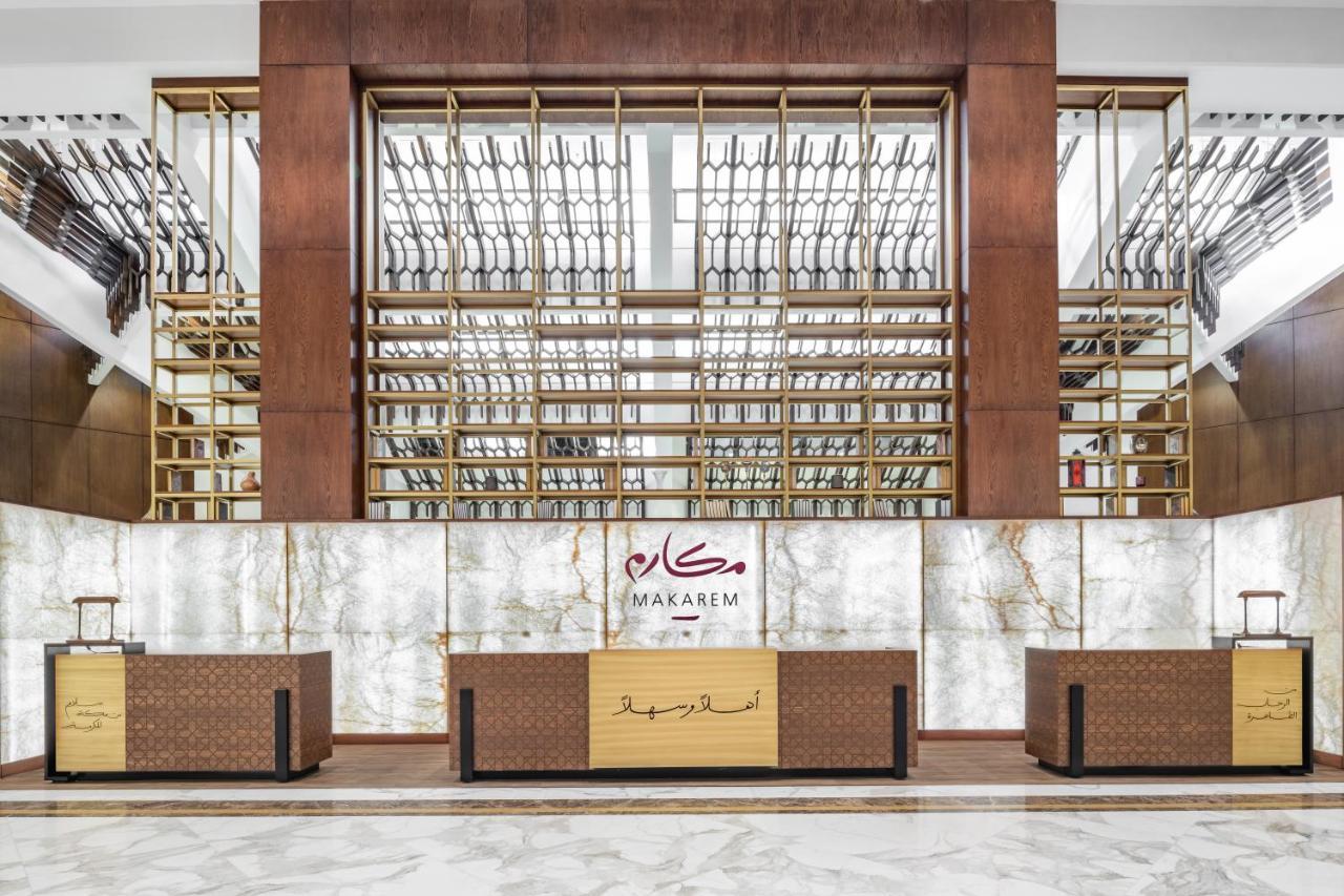 Makarem Ajyad Makkah Hotel La Meca Exterior foto The photo shows the interior of a hotel or a reception area, characterized by a modern and elegant design. In the foreground, there are multiple reception desks with a polished finish. Behind the desks, a striking feature is a wooden wall with a geom