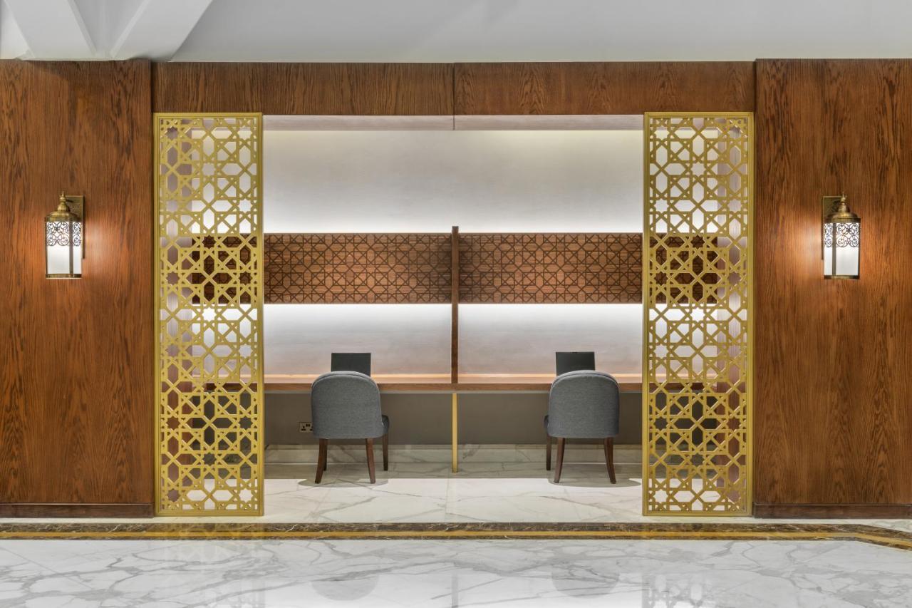 Makarem Ajyad Makkah Hotel La Meca Exterior foto The photo shows an elegantly designed space that features a reception or working area. There are two workstations with chairs positioned in front of them. The backdrop has a decorative panel with a geometric pattern. The area is framed by ornate gold