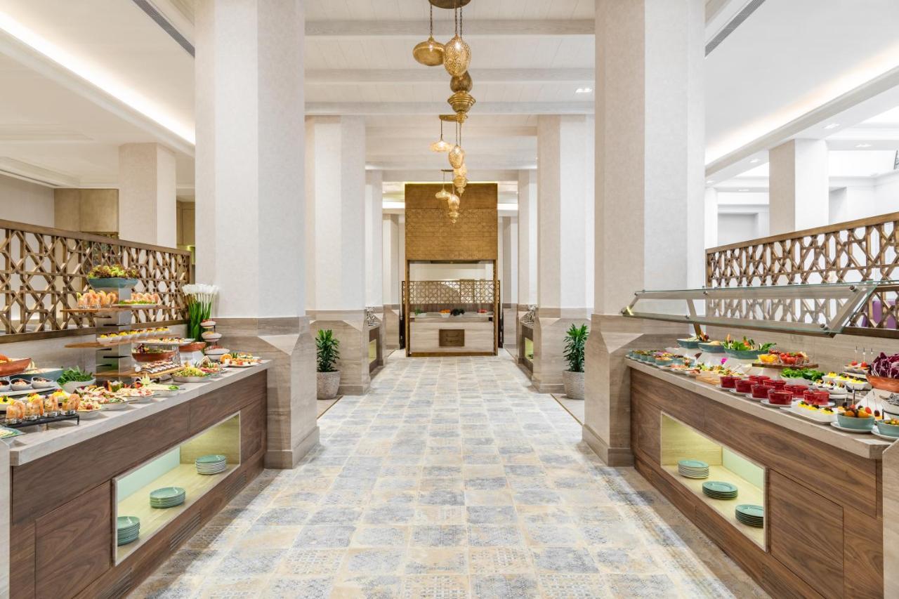 Makarem Ajyad Makkah Hotel La Meca Exterior foto The photo shows an elegant restaurant or buffet area. There are two long buffet tables on either side, displaying a variety of colorful dishes and desserts. The tables have an organized layout and are adorned with small plants. In the center of the r