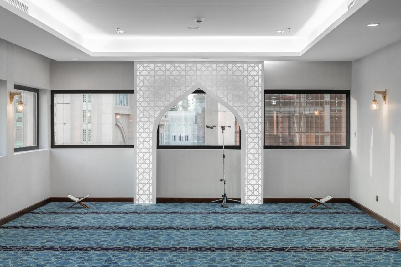 Makarem Ajyad Makkah Hotel La Meca Exterior foto The image shows a prayer room or small mosque interior. It features a white decorative wall with an archway that is typical in Islamic architecture. The floor is covered with a blue carpet, arranged with patterned lines, likely indicating prayer spot