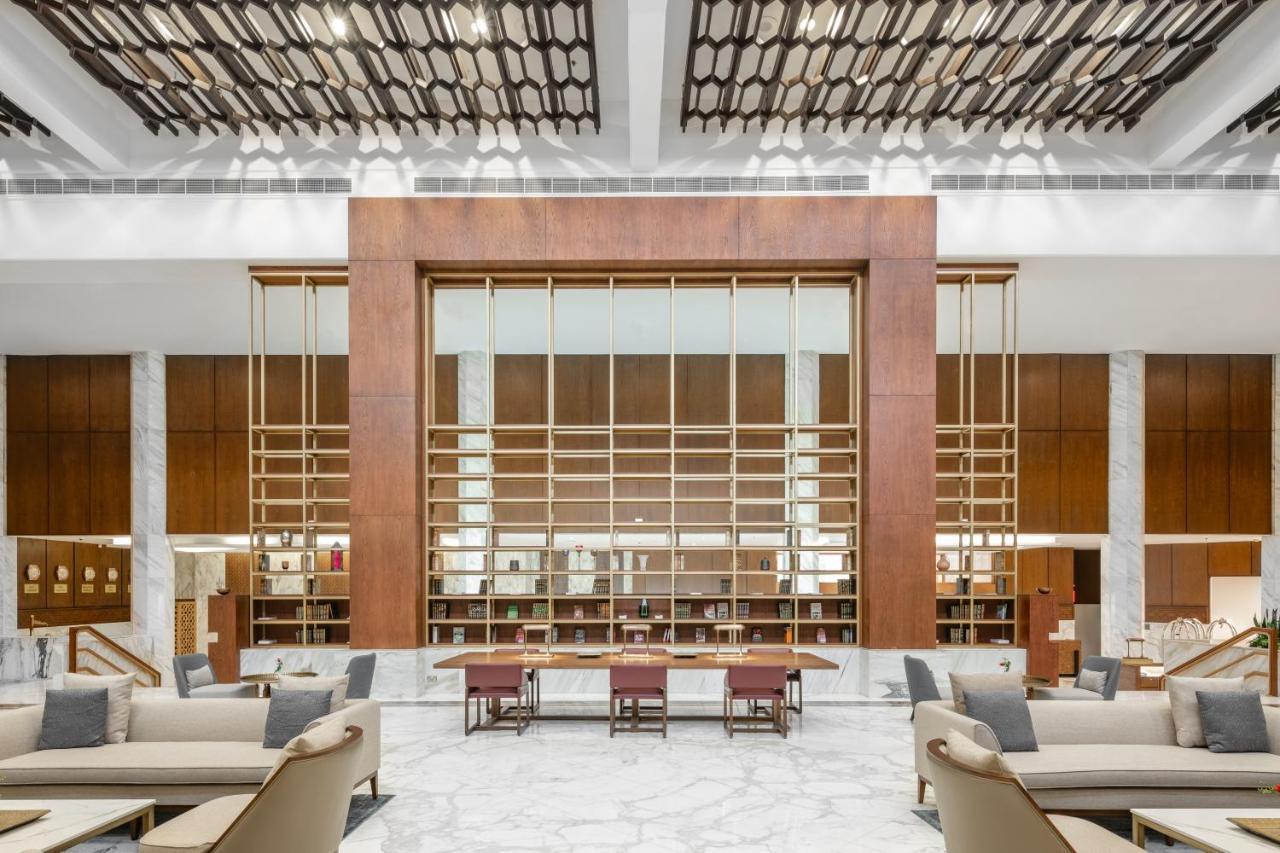 Makarem Ajyad Makkah Hotel La Meca Exterior foto The photo shows a spacious interior of a modern lobby or lounge. The design features a large wooden structure with a grid-like pattern in the center, possibly serving as a decorative partition. The walls are adorned with brown wooden panels, and marb