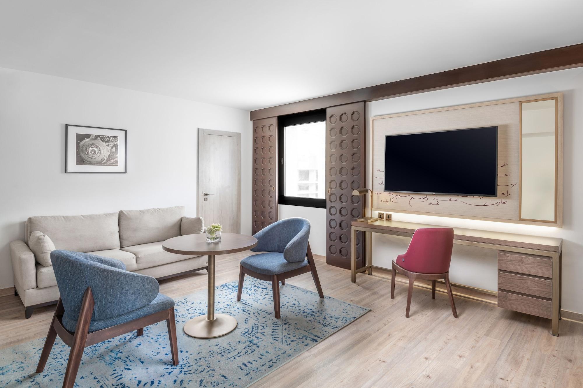 Makarem Ajyad Makkah Hotel La Meca Exterior foto The photo shows a modern living room setting. It features a light-colored sofa positioned against one wall, accompanied by a round table at the center. Two stylish chairs, one in blue and the other in pink, are placed around the table. There is a lar
