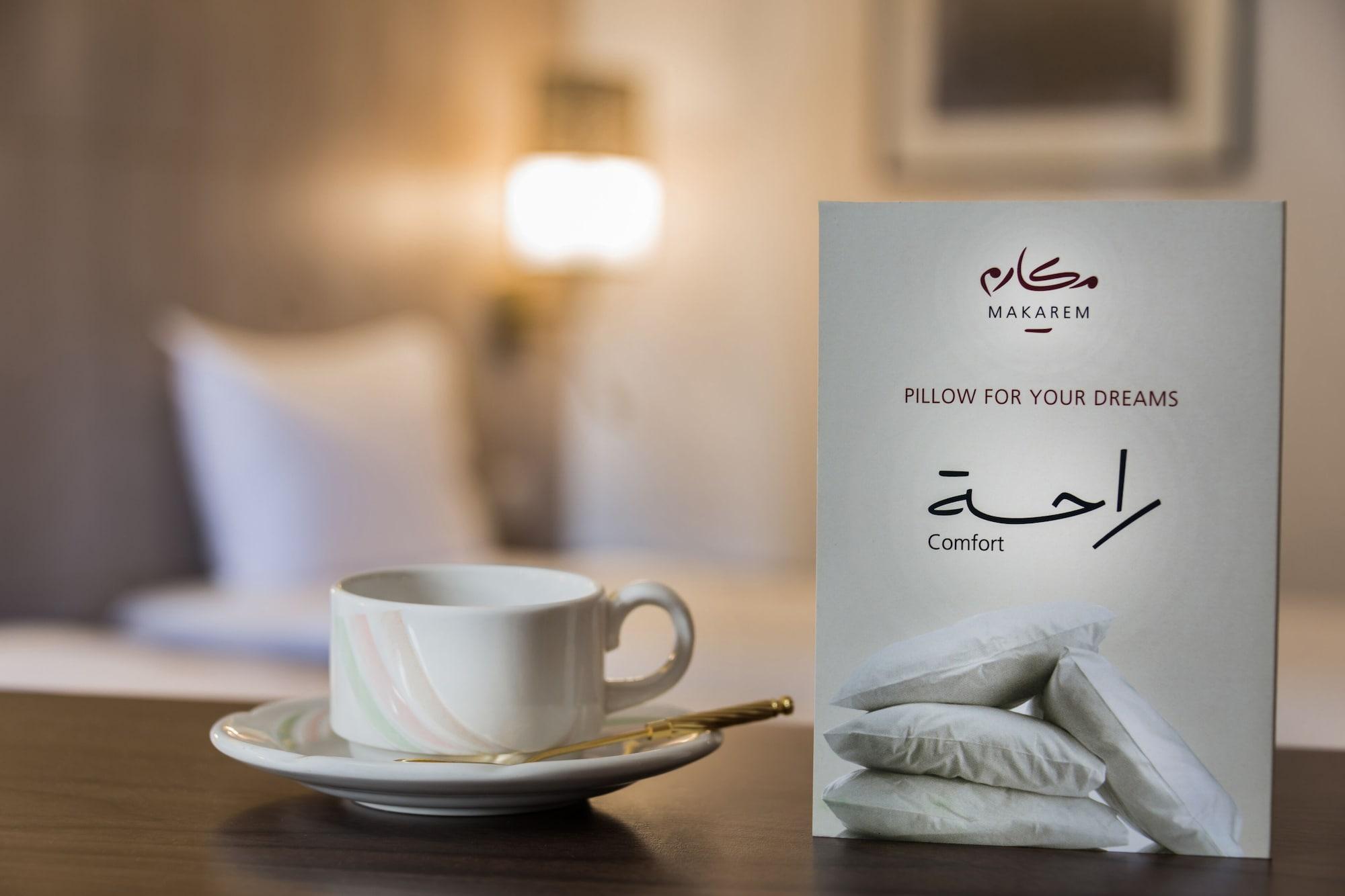 Makarem Ajyad Makkah Hotel La Meca Exterior foto The image features a cozy setting, likely a hotel room. In the foreground, there is a white cup of coffee or tea placed on a small saucer, accompanied by a gold spoon. Beside the cup is a decorative card or sign that reads "Pillow for Your Dreams" an