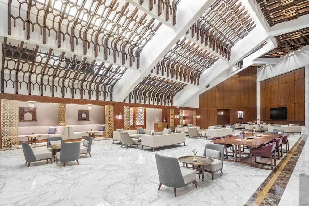 Makarem Ajyad Makkah Hotel La Meca Exterior foto The photo shows a spacious and elegantly designed lobby area, likely within a hotel. The interior features high ceilings with a unique architectural design, showcasing wooden elements arranged in a geometric pattern. The flooring is a polished marble