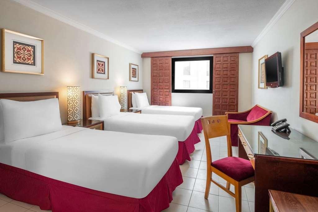 Makarem Ajyad Makkah Hotel La Meca Habitación foto The photo shows a hotel room featuring two twin beds with white linens and red bed skirts. There are decorative elements on the walls, including framed artwork. A large window provides natural light, while a desk and a chair are positioned next to it