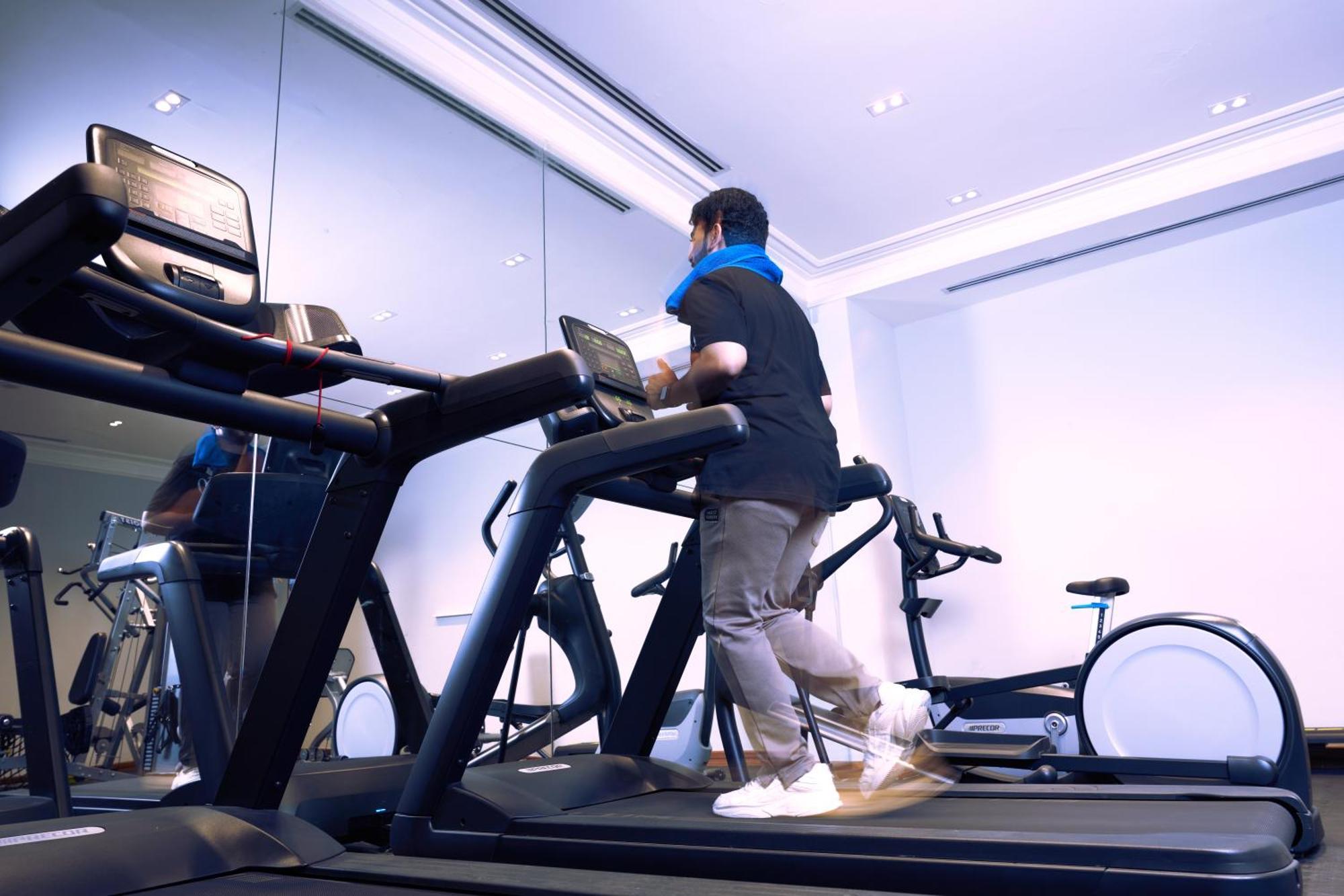 Makarem Ajyad Makkah Hotel La Meca Exterior foto The photo shows a person exercising on a treadmill in a modern gym or fitness room. The individual is wearing a blue neck support while jogging on the treadmill, which is set against a backdrop of large mirrors. There are also additional exercise equ