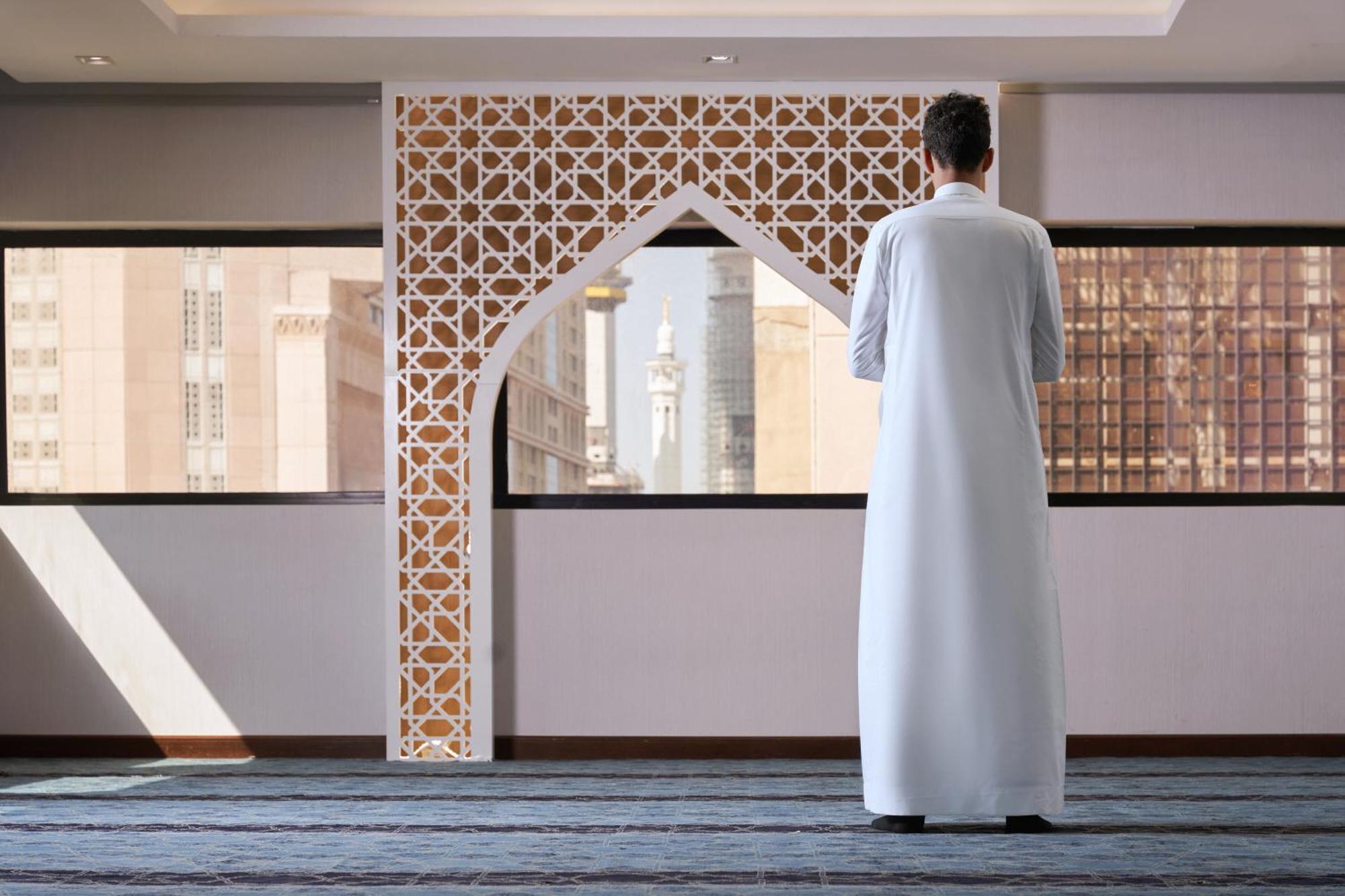 Makarem Ajyad Makkah Hotel La Meca Exterior foto The photo depicts a person standing with their back facing the viewer, wearing a traditional white garment. They are in a spacious interior setting that features an ornate archway with intricate patterns, typical of Islamic architecture. Through the 