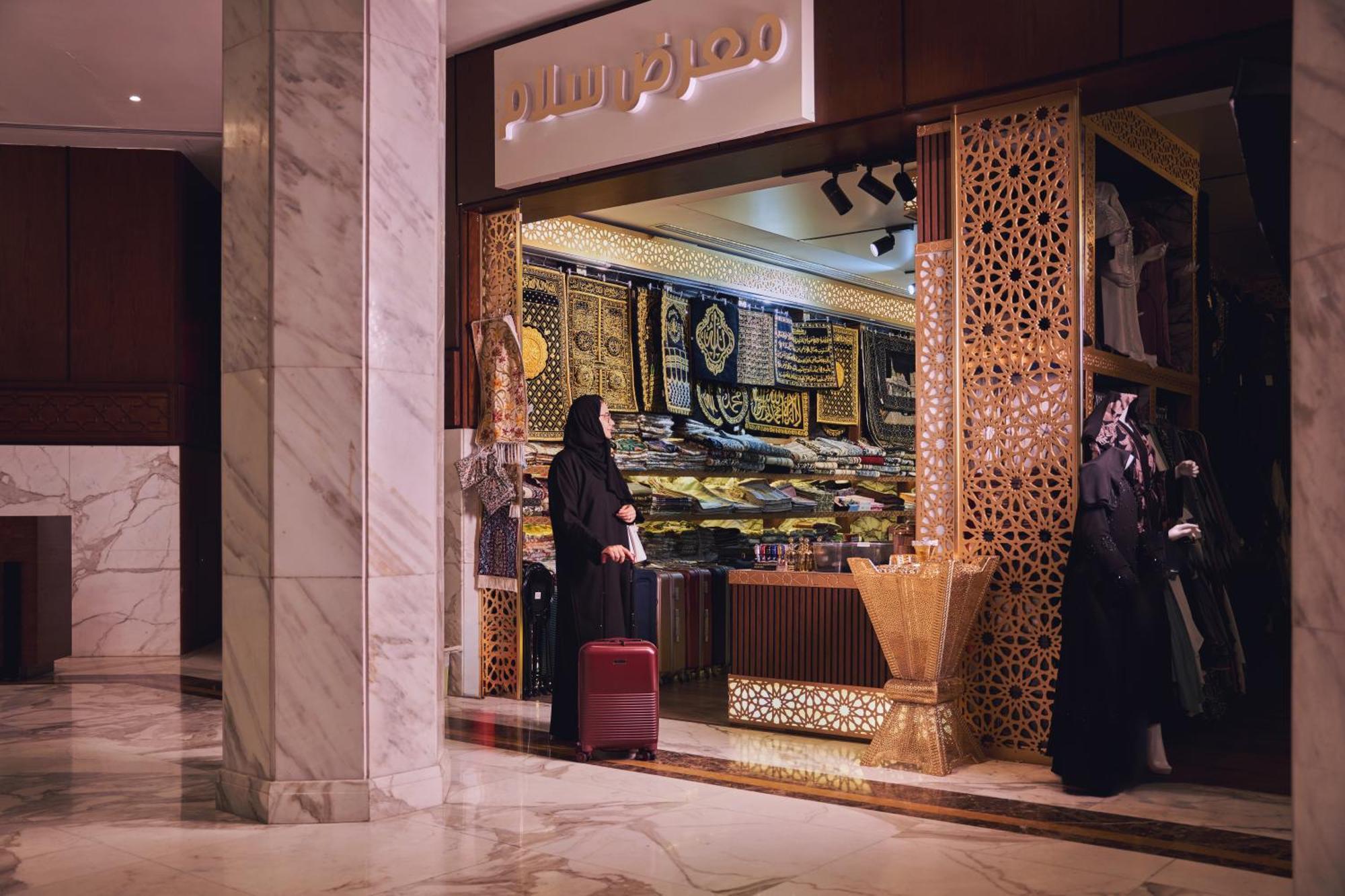 Makarem Ajyad Makkah Hotel La Meca Exterior foto The photo shows a storefront that appears to sell traditional textiles or garments. The entrance features intricate decorative patterns, typical of Middle Eastern architecture. A woman is standing outside the shop, dressed in a black abaya, and she h