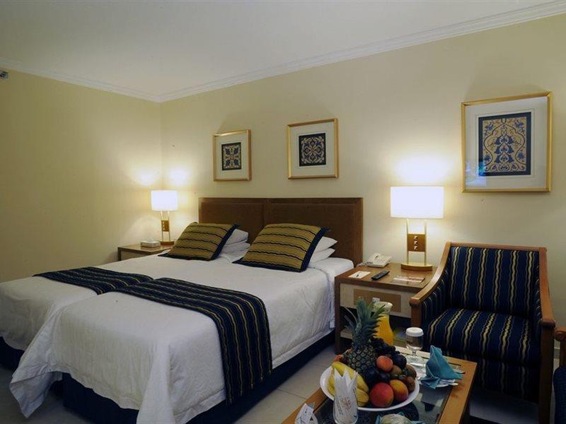 Makarem Ajyad Makkah Hotel La Meca Exterior foto The photo shows a hotel room with a cozy and inviting atmosphere. It features two beds with white linens and dark striped bedspreads. There are two bedside lamps providing warm light, and the walls are decorated with framed artworks. Beside the beds 