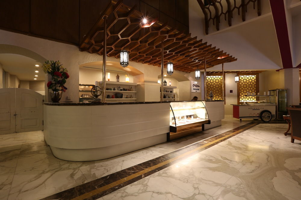 Makarem Ajyad Makkah Hotel La Meca Exterior foto The photo shows a modern reception area or lobby of a hotel or restaurant. The focal point is a curved front desk made of white material, featuring a glass display case that showcases various items. Above the desk, there is a decorative wooden struct